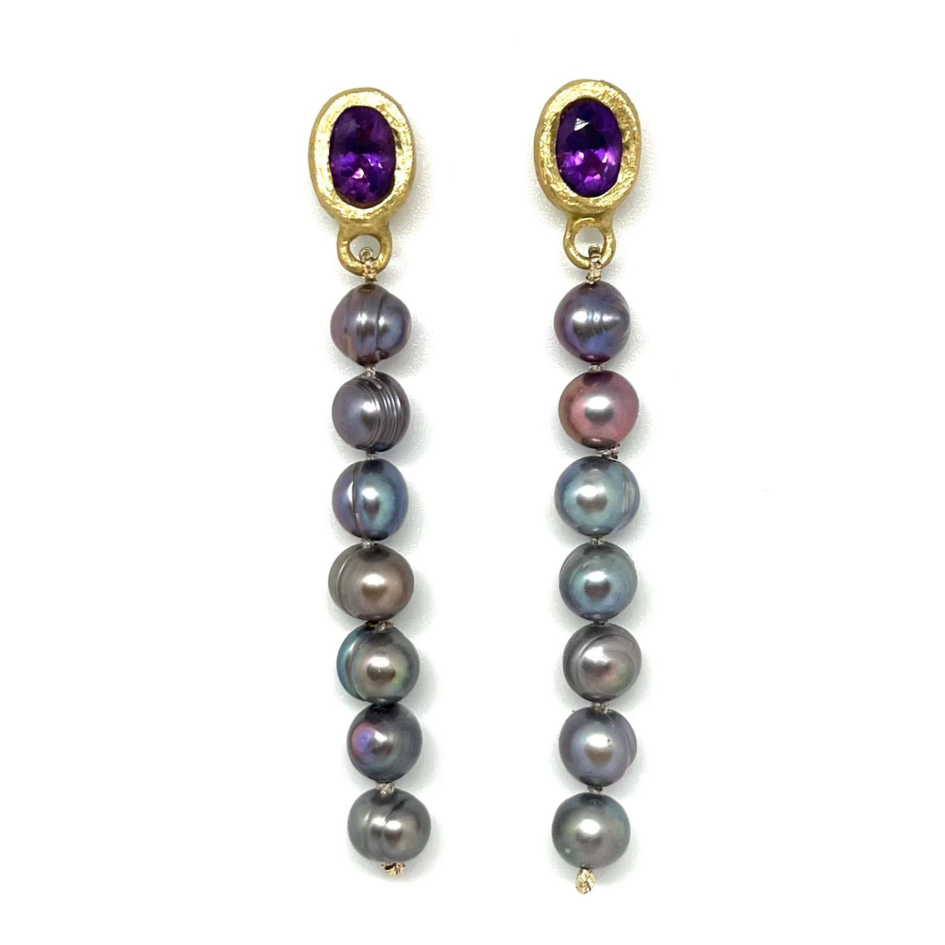 A pair of gold dangle earrings featuring oval purple amethyst tops and a vertical drop of dark gray and iridescent baroque pearls, set against a plain white background.